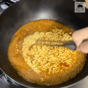 トングでラーメンをかき混ぜながら調理するシーン