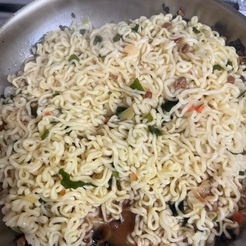 Mixing the spaghetti and raccoon noodles with the sauce in the pan.