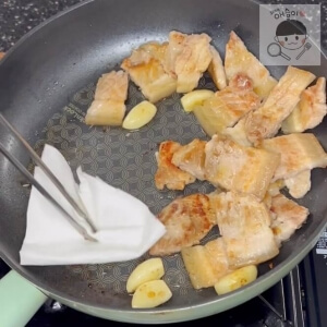 油を取り除くためにキッチンタオルで豚バラ肉のフライパンを拭く様子。