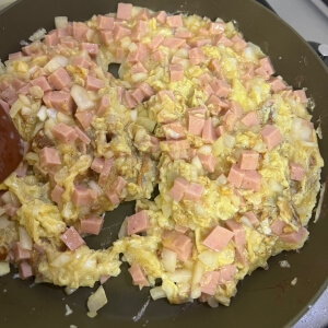 フライパンでスパムと玉ねぎを入れた卵のスクランブルを炒める様子