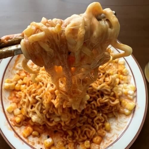 Corn cheese bulgogi noodles picked up with chopsticks. The cheese is stretching