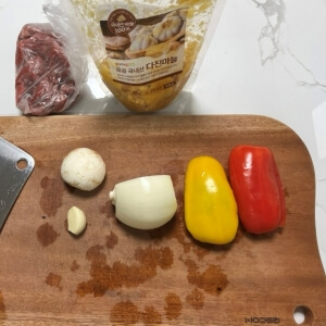 재료 준비 이미지: 찹스테이크 재료(소고기, 다진 마늘, 양파, 파프리카, 버섯)를 도마 위에 올려둔 모습.