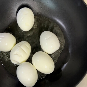 フライパンにゆで卵を入れて焼き始めるシーン