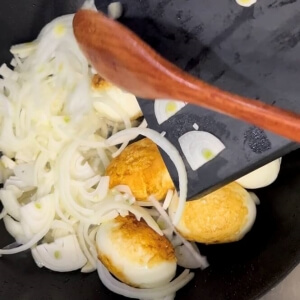 黄金色に焼いた卵と一緒に玉ねぎをフライパンに入れるシーン