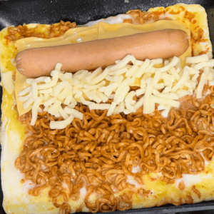 ブルドック焼きそばの上にチェダーチーズ、ソーセージ、モッツァレラチーズをのせた様子。