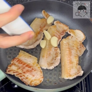 焼かれる豚バラ肉の横にニンニクを追加する様子