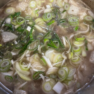 沸騰している牛肉の煮汁に最後にネギを加えて風味を加える様子。