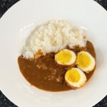 たまごカレーのレシピを完成させたところ。 白い皿の上に白米が乗せられ、その横に濃い茶色のカレーがたっぷりと置かれている。その上には、半分にカットされたゆで卵が3個置かれている。卵の断面が美味しそうに出ている。