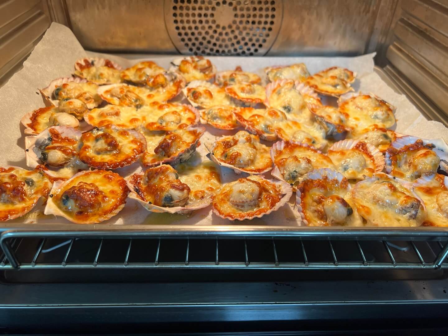 La receta de vieiras con queso terminada. El horno está repleto de vieiras doradas al horno con queso.