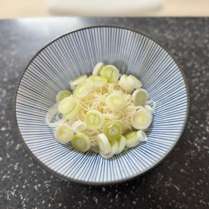 A bowl with boiled somen noodles and sliced scallions.