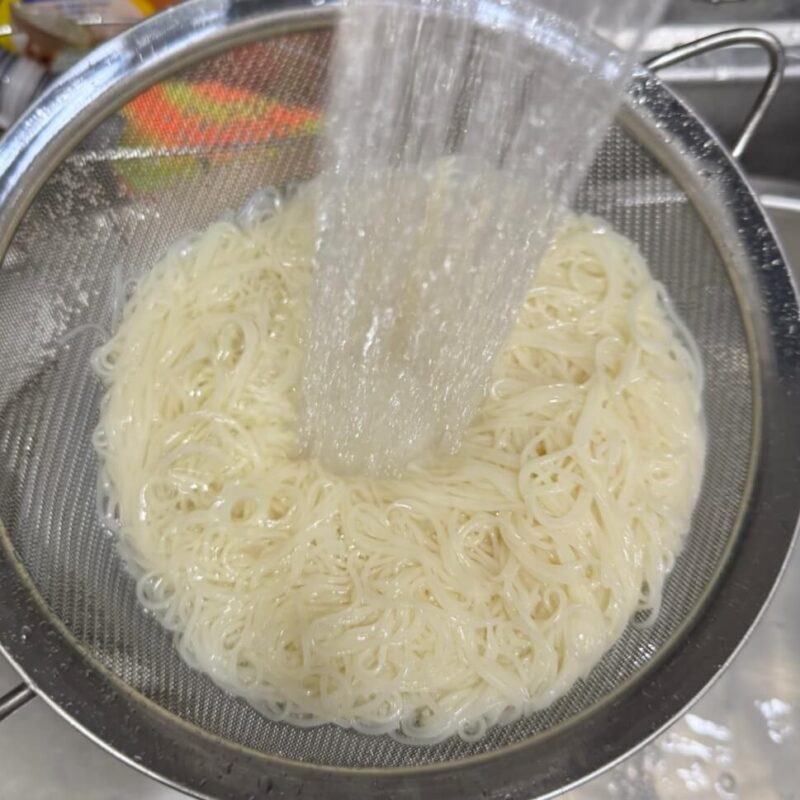 Boiled somen noodles being rinsed under cold water.