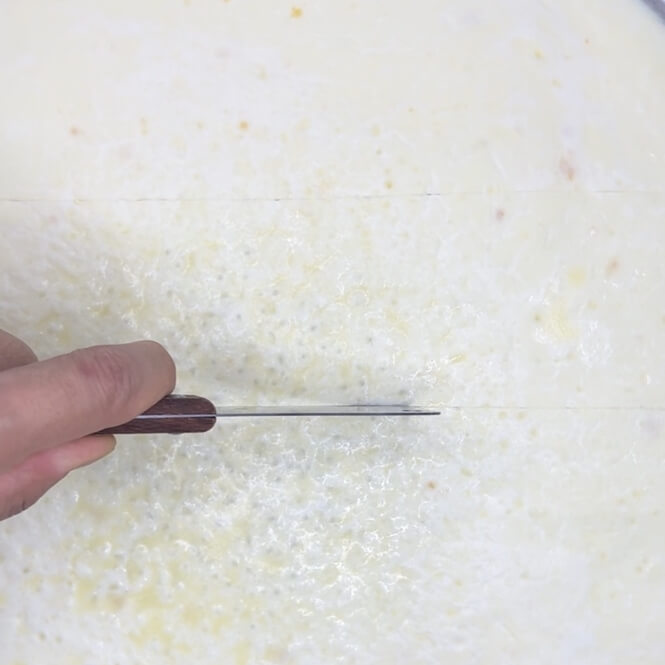 Cutting the cooled kaimak with a knife on a large pan.