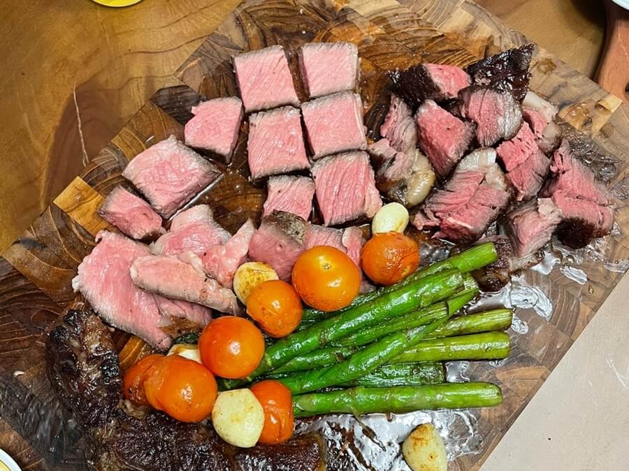 リバースシアリングステーキの焼き方を完成させた姿で、トマホークを一口大に切り、付け合わせの野菜と一緒にまな板の上に乗っている様子。