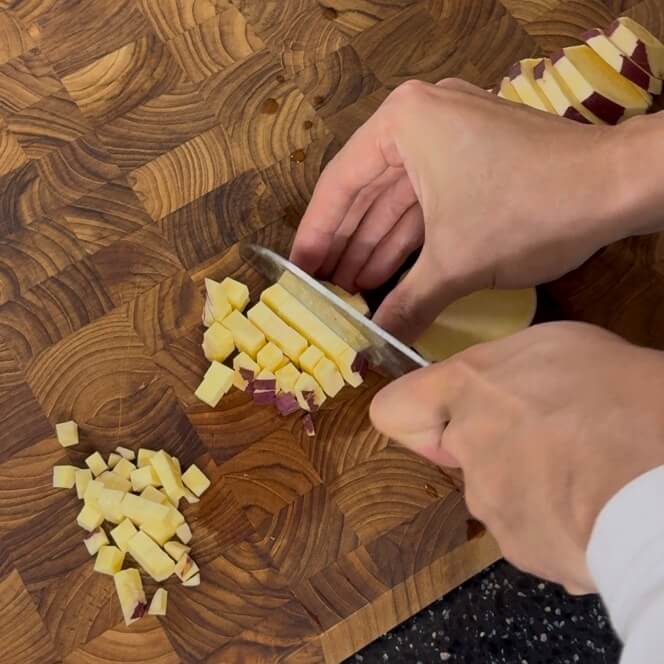 Stacking cut sweet potatoes and cutting them into small cubes.