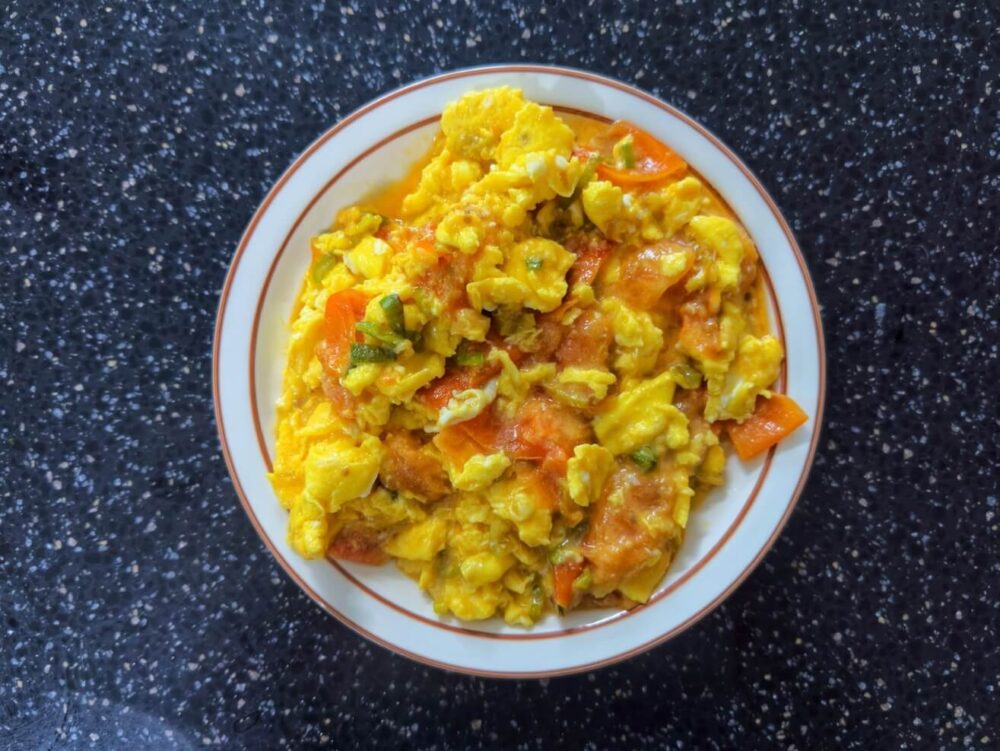 The finished product of this moist tomato fried egg recipe is a white plate of moist, cooked eggs and tomatoes.