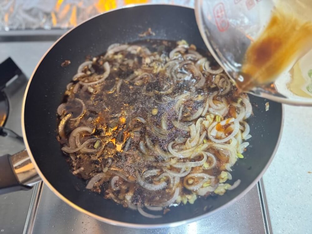 炒めた玉ねぎに醤油ソースをかける様子