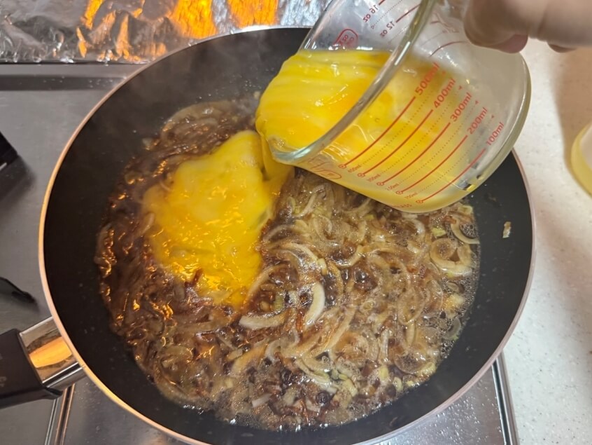 煮込んだ醤油の上に卵液を注ぐ様子