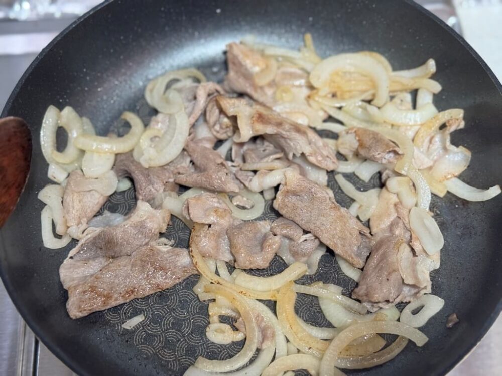 フライパンの中の玉ねぎと大判豚バラ肉が茶色く焼けた様子