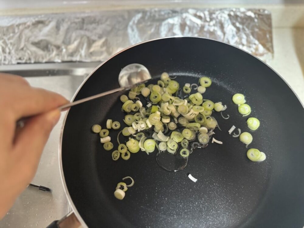 フライパンのネギで食用油を入れる様子