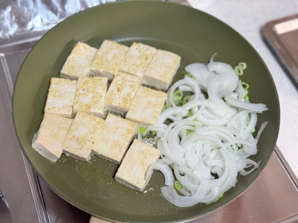 豆腐とカットした野菜を一緒にフライパンで調理する様子。