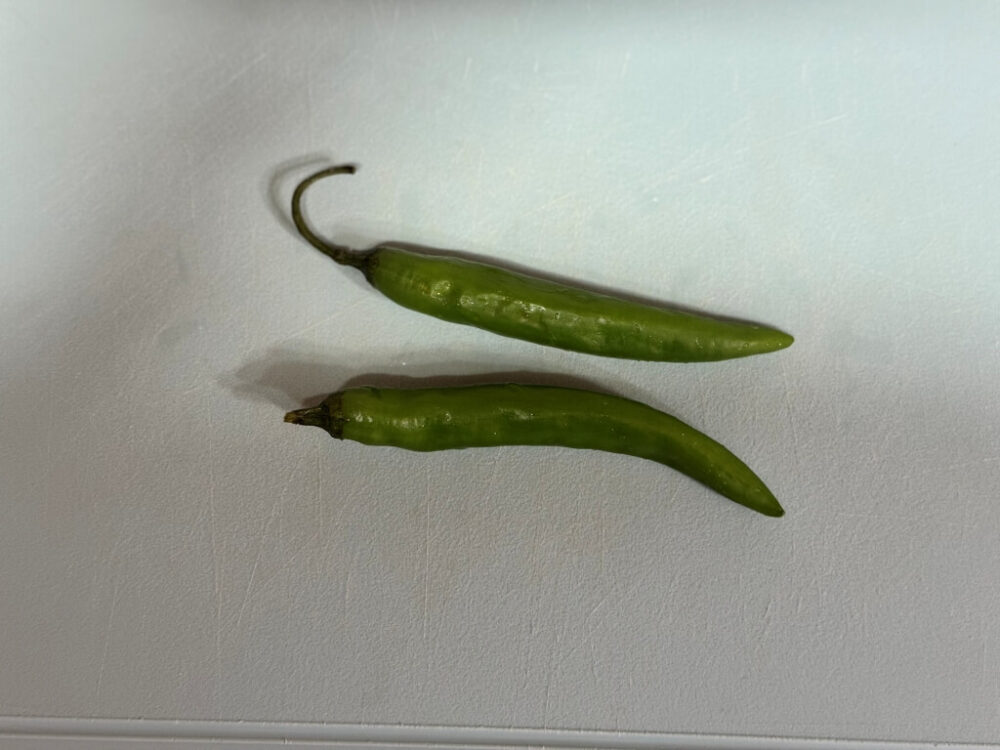 Two green and red peppers on a cutting board.