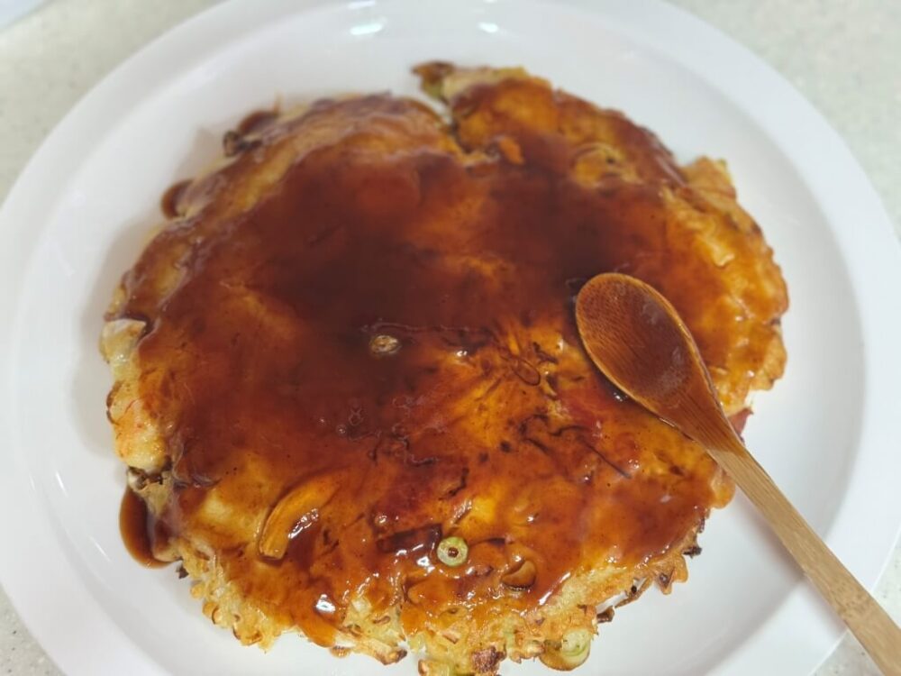 Transferring okonomiyaki to a plate and brushing with teriyaki sauce.