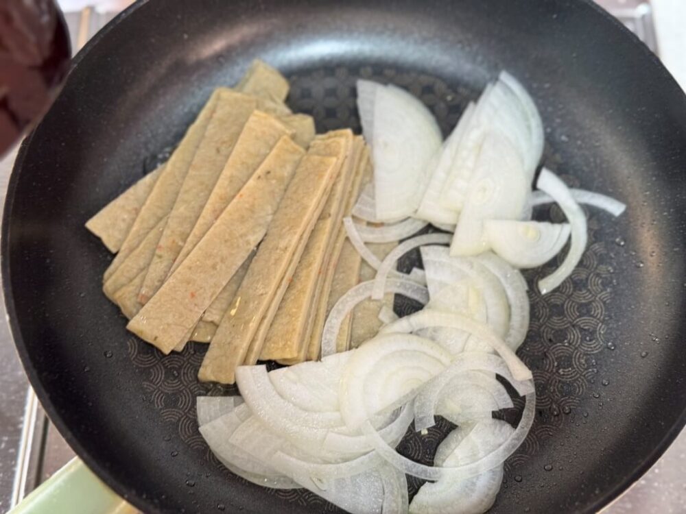 Los pasteles de pescado recortados y las cebollas en la sartén.