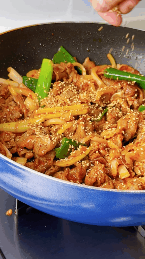 Sprinkling sesame seeds to finish off the jeyuk stir-fry recipe.